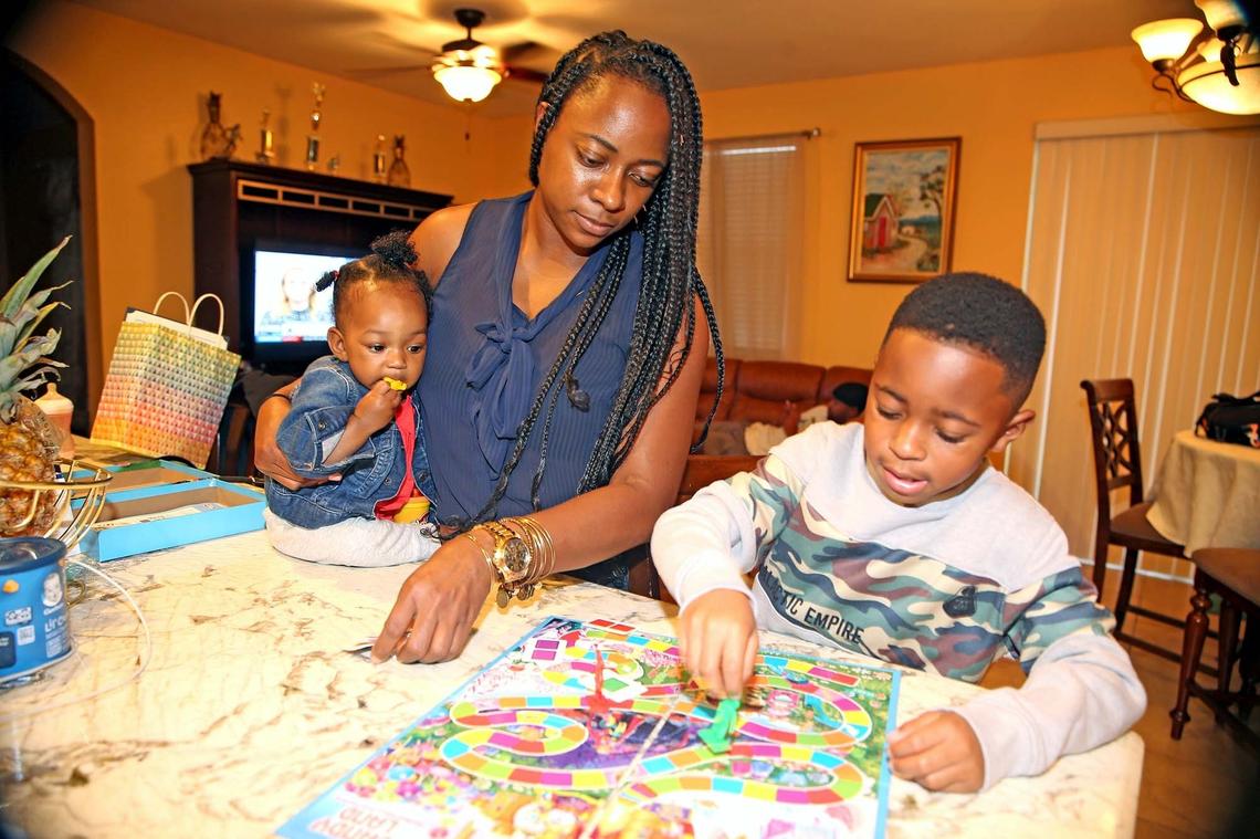 Lasonya Rogers and her son Aiden 7, and her daughter Aubrielle, 8 months, play a board game in her mother’s Homestead house, June 13, 2019. Lasonya and her family are living with her mother to save money and buy their own home.