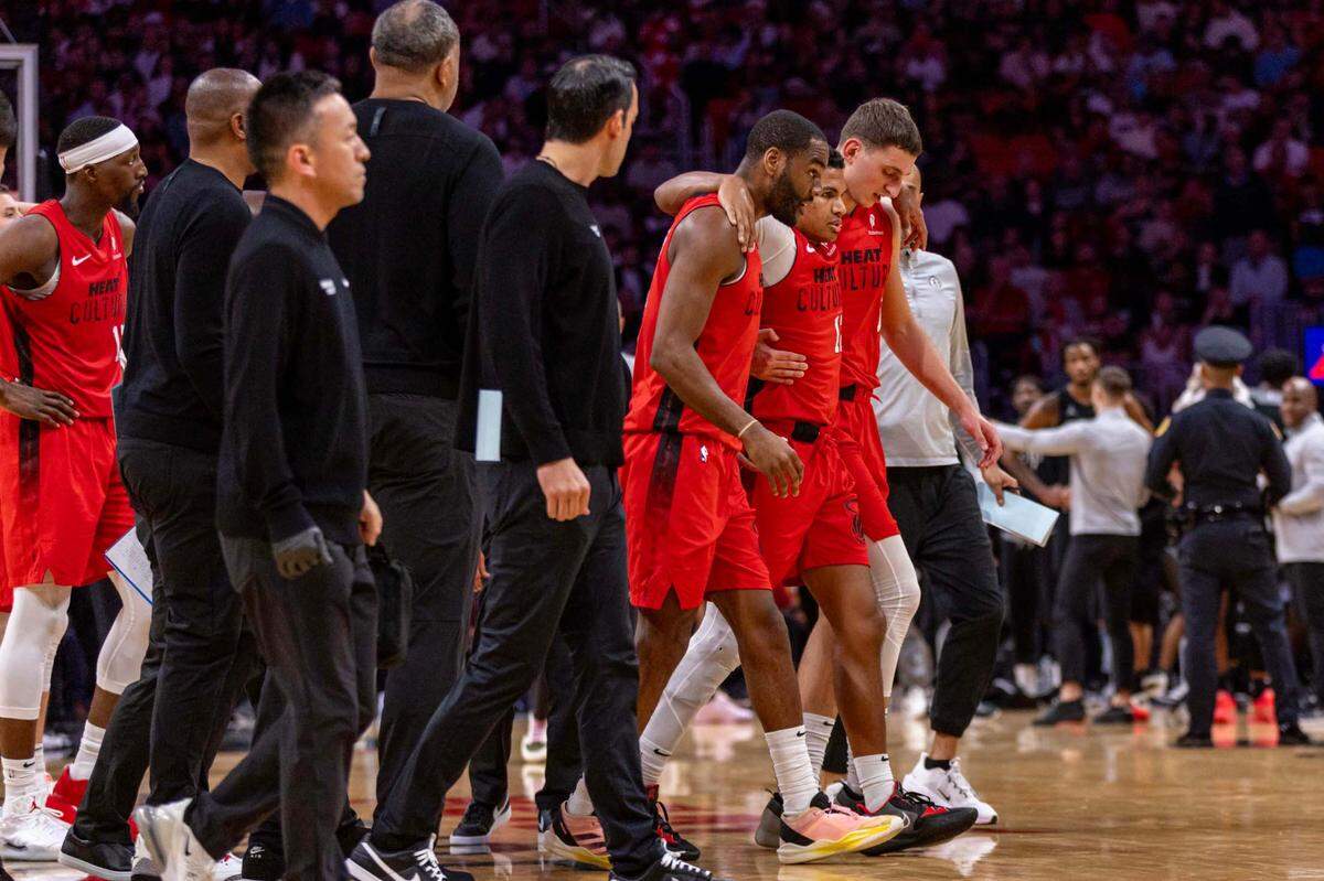 Miami Heat guard Dru Smith (12) is carried off the court by teammates Nikola Jovic (5) and Alec Burks (18) after being injured on a play during the first half of an NBA game against the Brooklyn Nets at Kaseya Center on Monday, Dec. 23, 2024, in Miami.