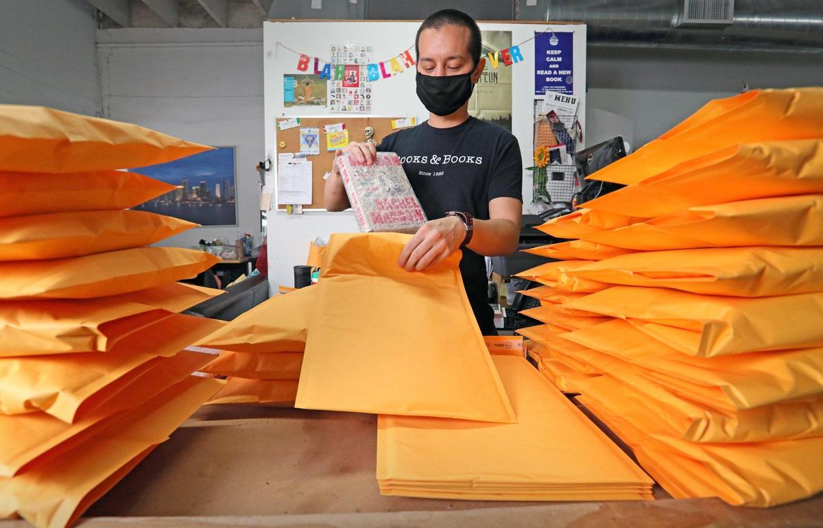 Books & Books employee Sean Bauza packs books in envelopes as he fulfills holiday orders that are shipping out of the company warehouse on Thursday, December 17, 2020.