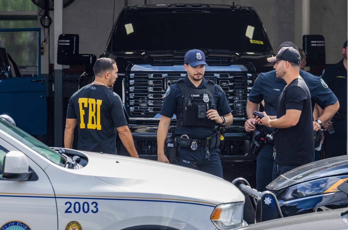 Police and federal agents talk to an unidentified man (far right) during their raid of Doral Collision on Friday, Aug. 16, 2024. The raid was in connection with the Aug. 27, 2019, plot to kill Alex Vega, a famed Miami car designer, who survived the hit attempt.