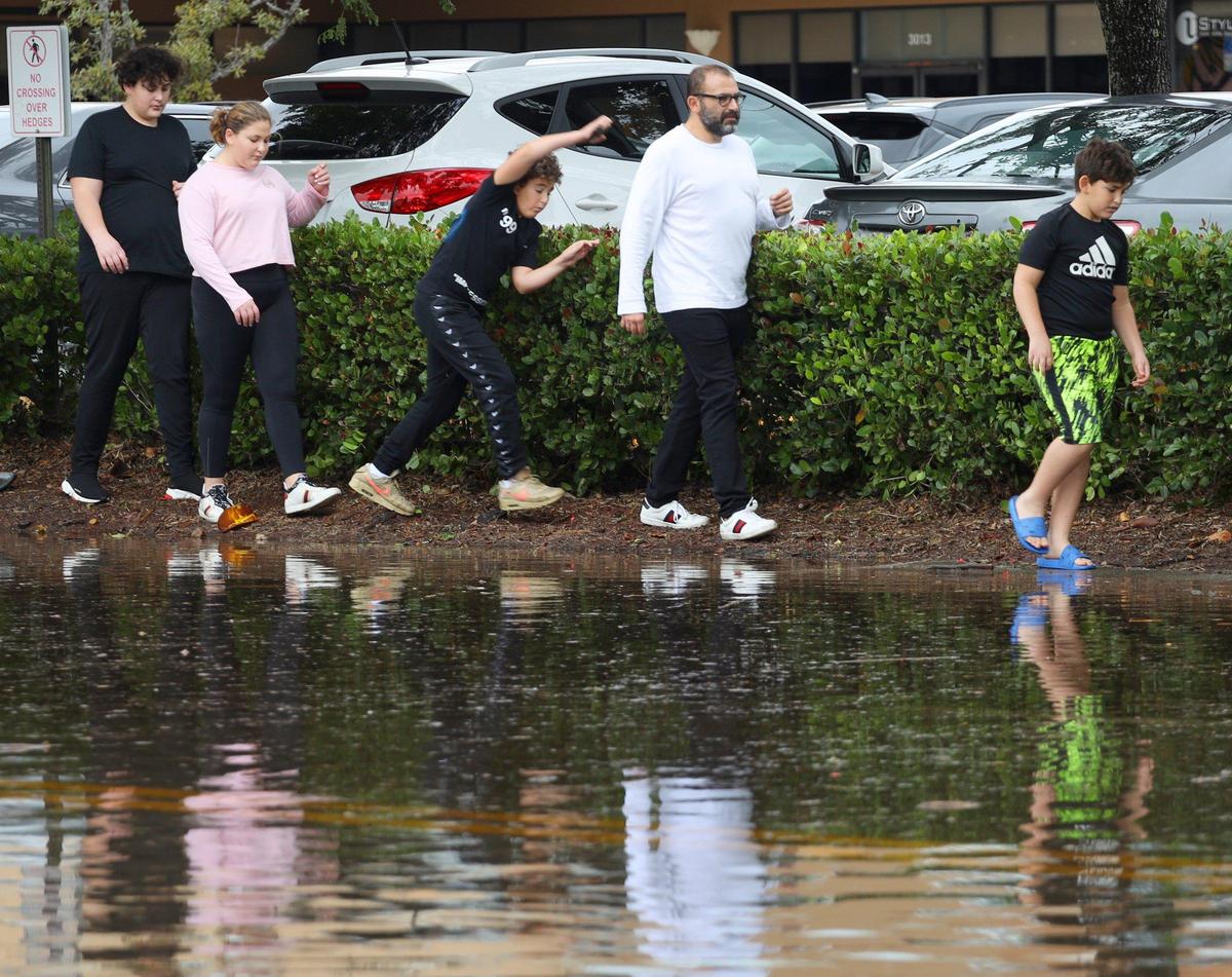 Family members try to keep their feet dry while walking across the street to the Biscayne Lake Gardens apartment complex, where surrounding streets were flooded by late night and early morning downpours in Aventura, Florida, on Monday, December 23, 2019.