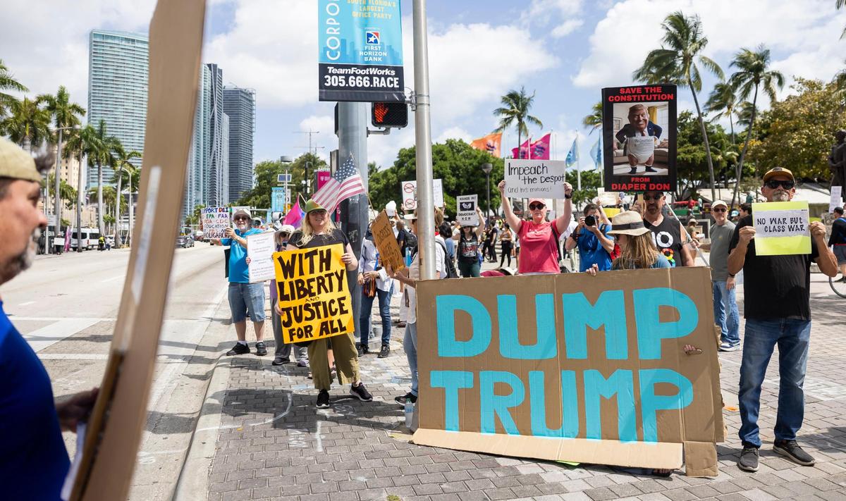 Activists hold signs and chant during a National Day of Action protest against President Donald Trump and his administration at the Torch of Friendship on Saturday, April 19, 2025, in downtown Miami, Fla.
