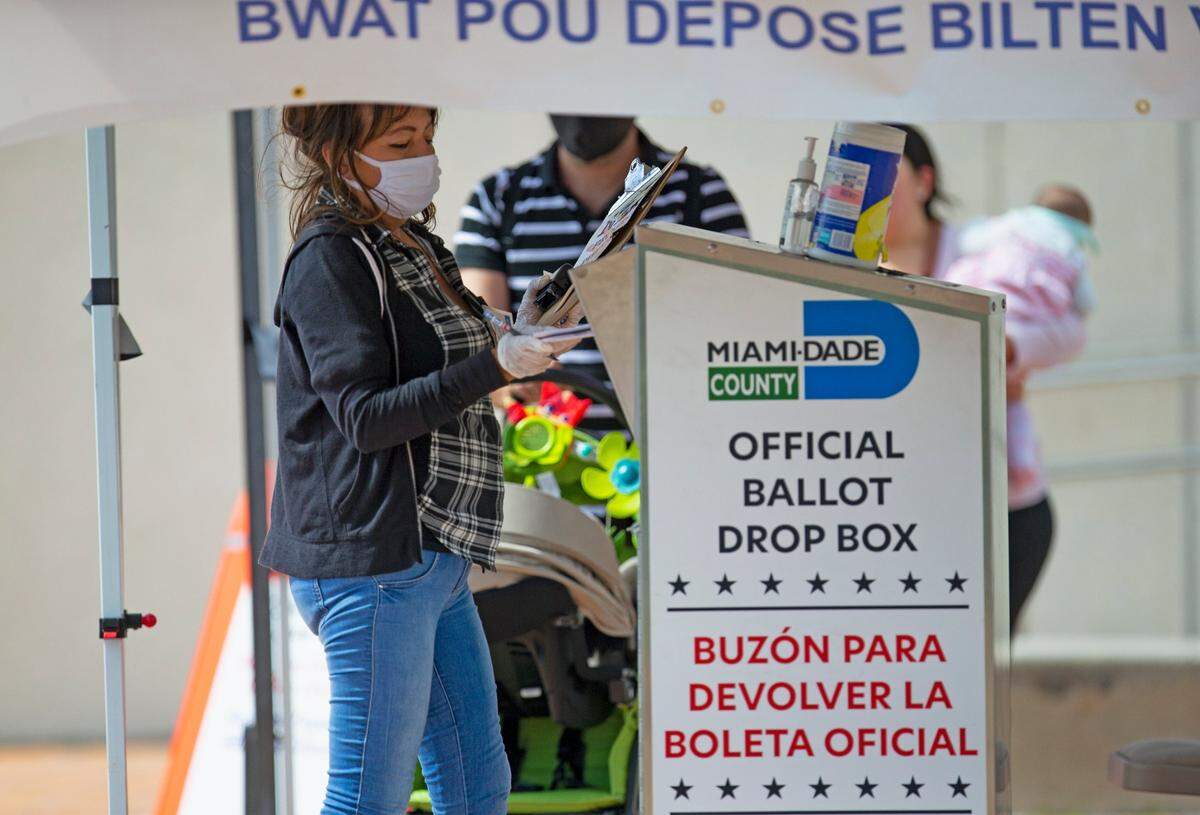 A polling worker deposits ballots at the official drop box outside the Westchester Regional Library during early voting for the general election on Wednesday, October 28, 2020 in Miami.