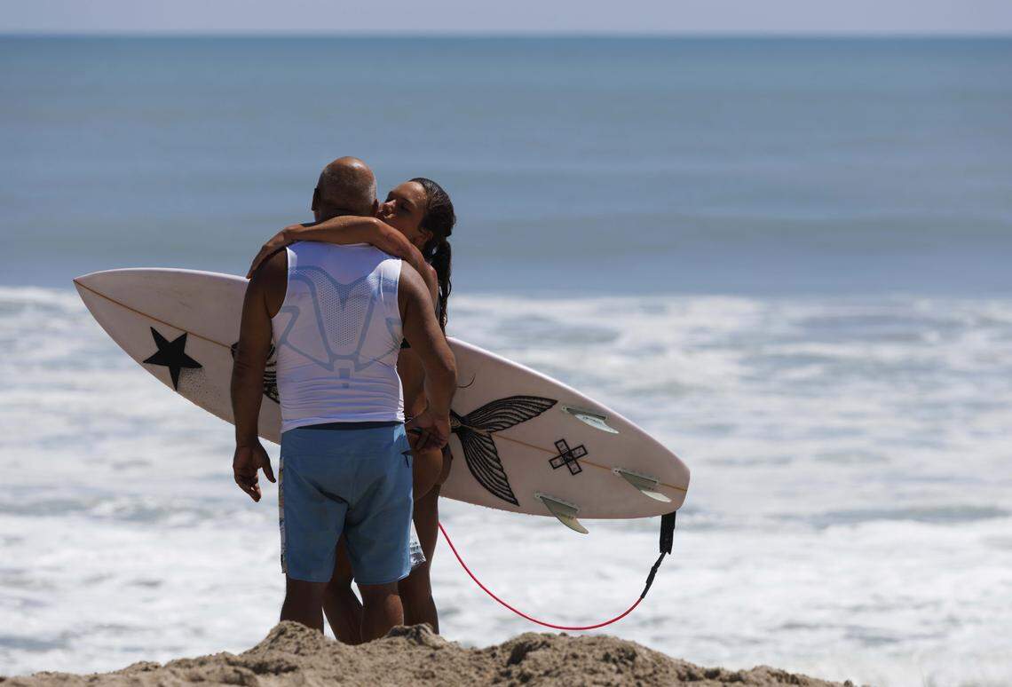 Isabella Dimain, 19, right, kisses her father on the cheek during the morning on Thursday, Aug. 21, 2025, off the beach in Stuart, Fla. He drove down the coast to come see her surf.