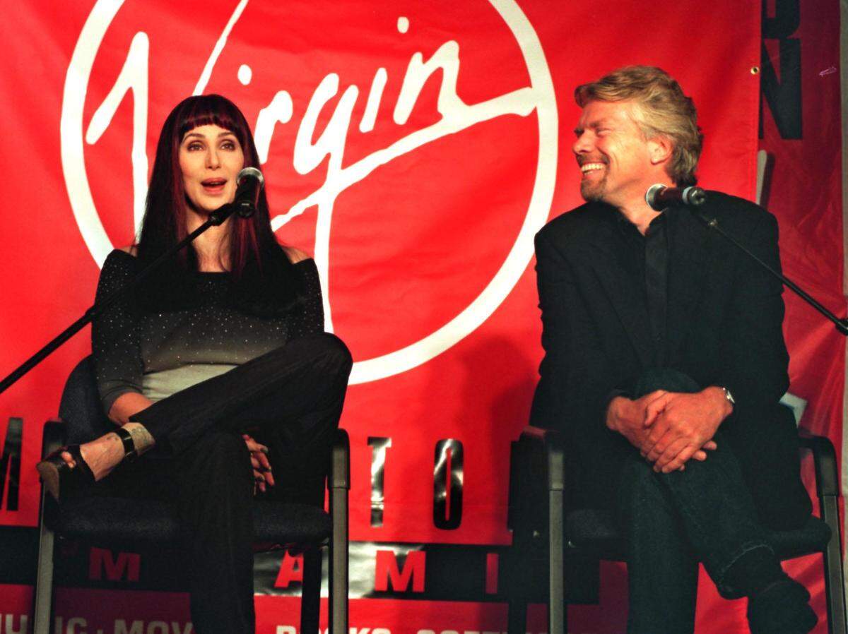 En esta foto del 29 de enero de 1999, la superestrella Cher y Richard Branson, fundador y presidente de Virgin Records, saludan a los fans frente al logotipo de Virgin en la tienda Virgin Megastore en The Shops at Sunset Place, donde se llevó a cabo una gran ceremonia de inauguración y de corte de cinta del Super Bowl. Cher estaba en el sur de Florida para promocionar su exitoso álbum, “Believe”, en la tienda de discos y ese fin de semana cantó el himno nacional en el Super Bowl en Miami Gardens, en lo que ahora se llama Hard Rock Stadium.