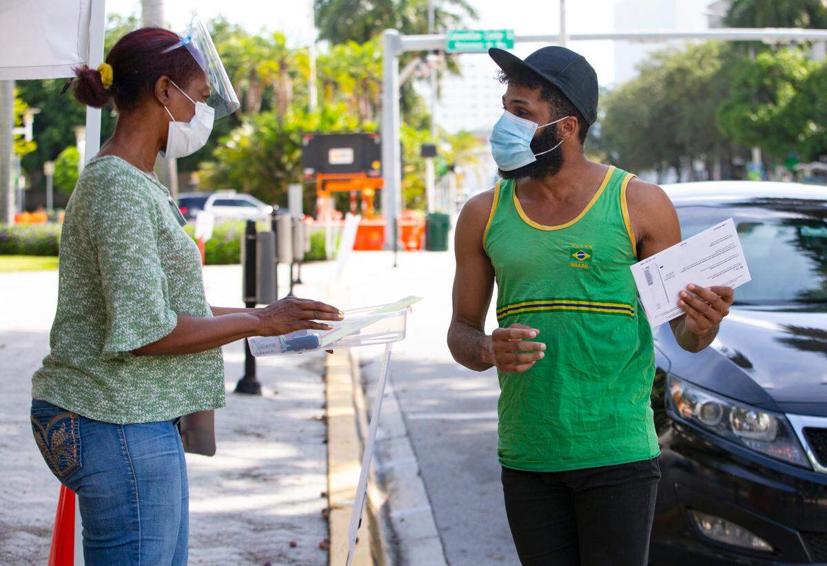A poll worker talks to Miami-Dade resident James Curity at the official drop box outside the Miami Beach City Hall during early voting for the general election on Wednesday, Oct. 28, 2020, in Miami Beach.