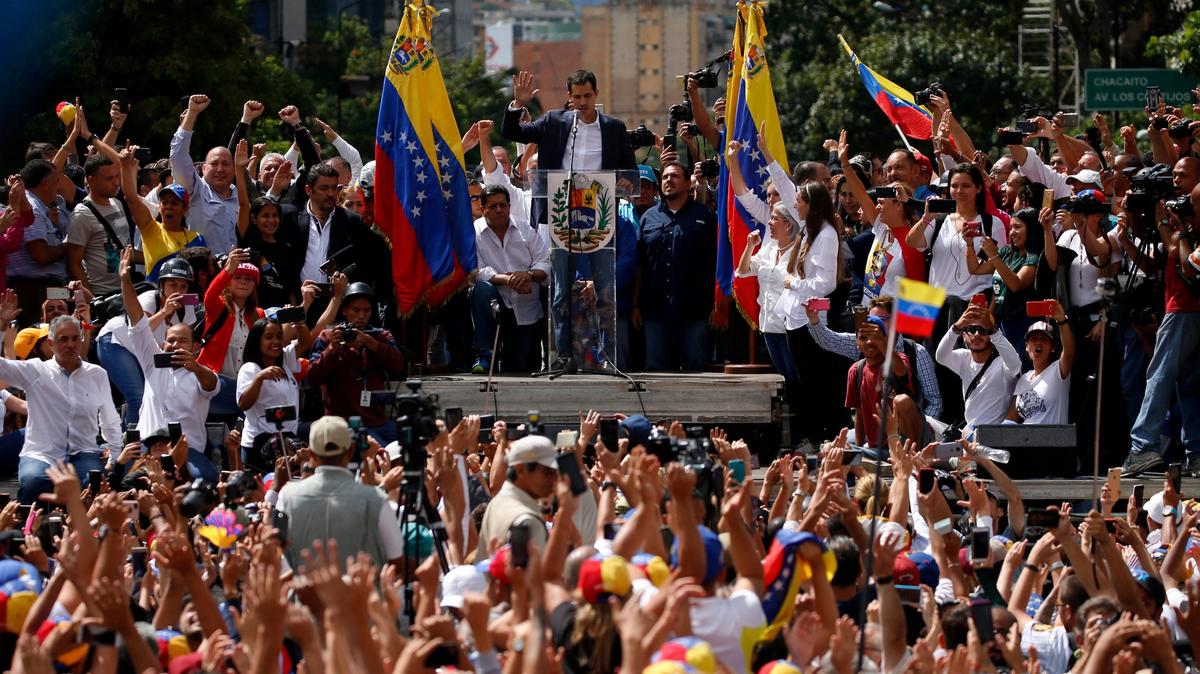 Juan Guaido, head of the opposition-run congress, looks down and holds up his hand during his symbolic swearing-in as interim president of Venezuela on a stage during a rally demanding President Nicolas Maduro’s resignation in Caracas, Venezuela, Wednesday, Jan. 23, 2019. Guaido declared himself interim president. (AP Photo/Fernando Llano)