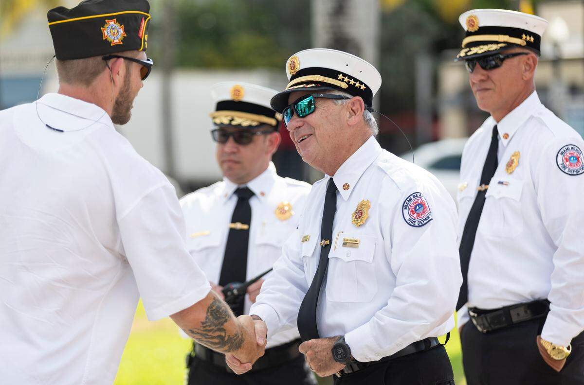 Miami Beach Fire Chief Virgil Fernandez, center, shakes hands with a U.S. Marine Corps. veteran before the start of a Memorial Day commemoration at the Miami Beach Police Headquarters on Monday, May 27, 2024, in Miami Beach.