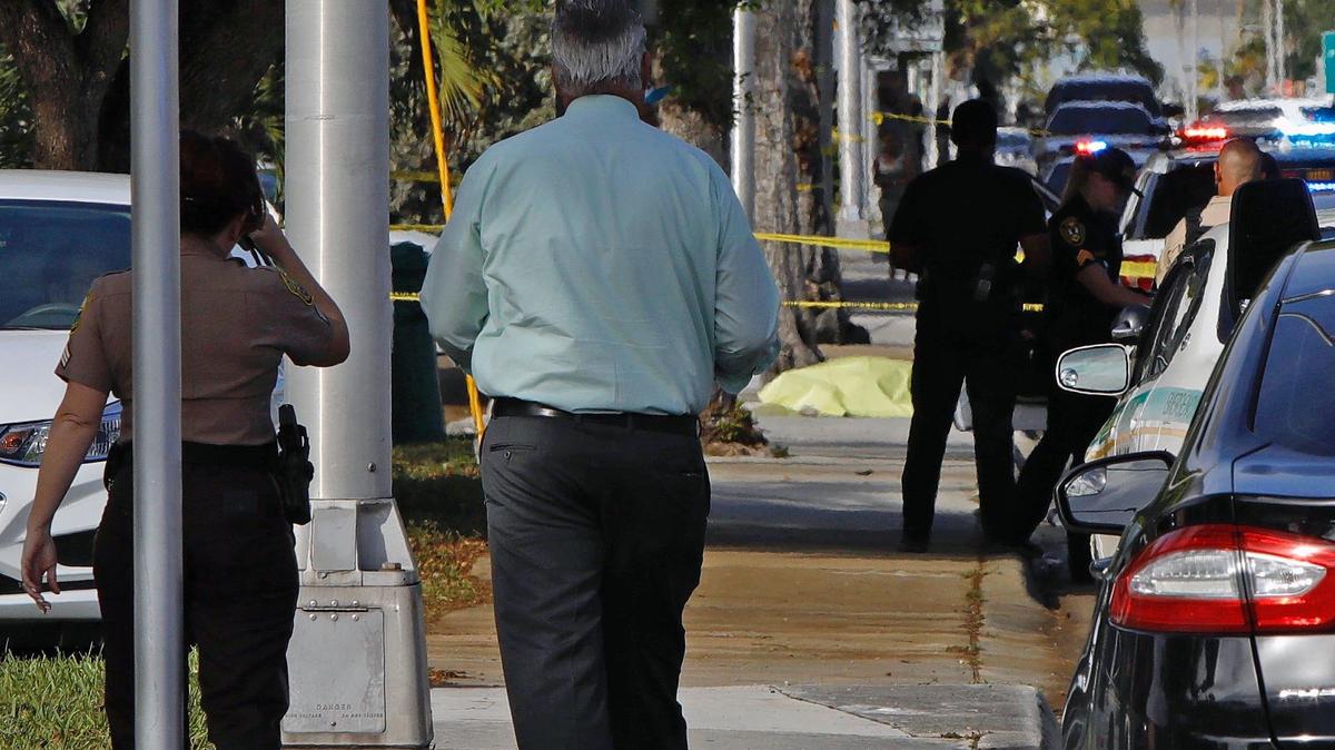 A body lies on the sidewalk near the intersection of Northeast Second Avenue and 119th Street where a Miami-Dade Police officer was injured after a police-involved shooting in North Miami Saturday afternoon.