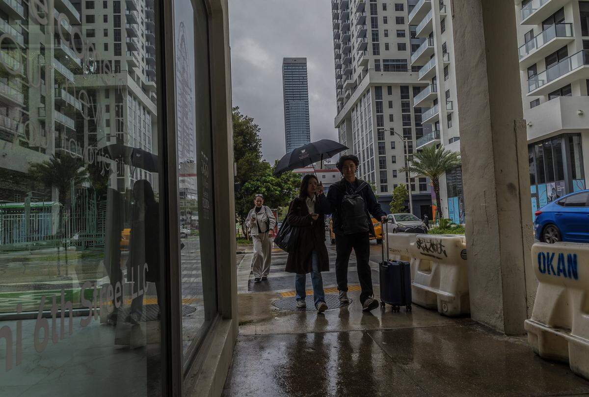 A couple takes cover as they walk along North Miami Avenue during a cloudy morning. The National Weather Service predicts rain chances near 50%, during the afternoon, on Wednesday, March 18, 2026.