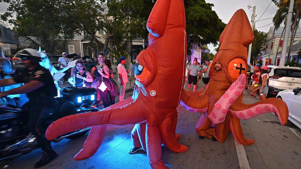 A police officer rides past two revelers costumed as squids during the Captain Morgan Masquerade March Friday, Oct. 27, 2023, in Key West.