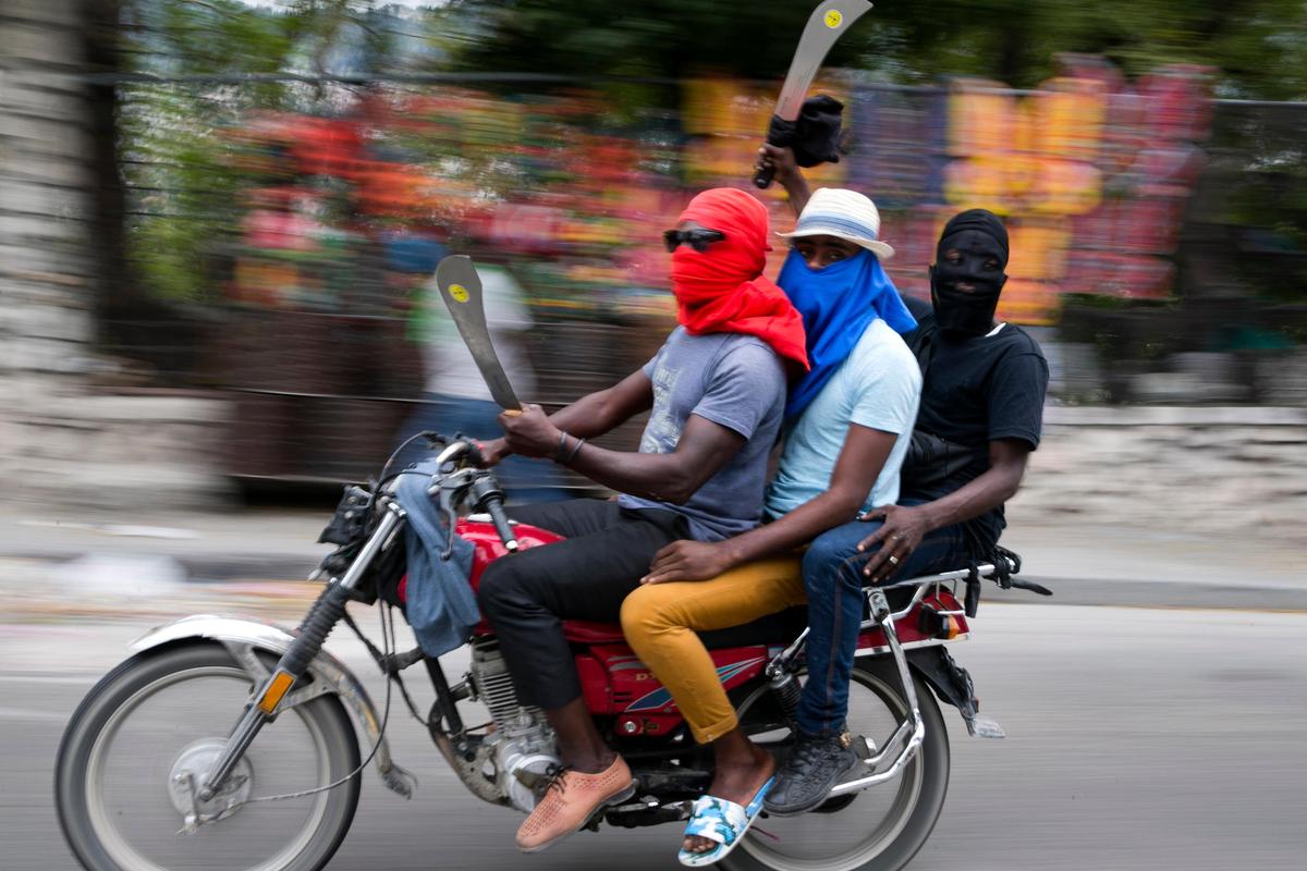 Men on a motorcycle brandish machetes as off-duty police officers protest over pay and working conditions, in Port-au-Prince, Haiti, Monday, Feb. 24, 2020.
