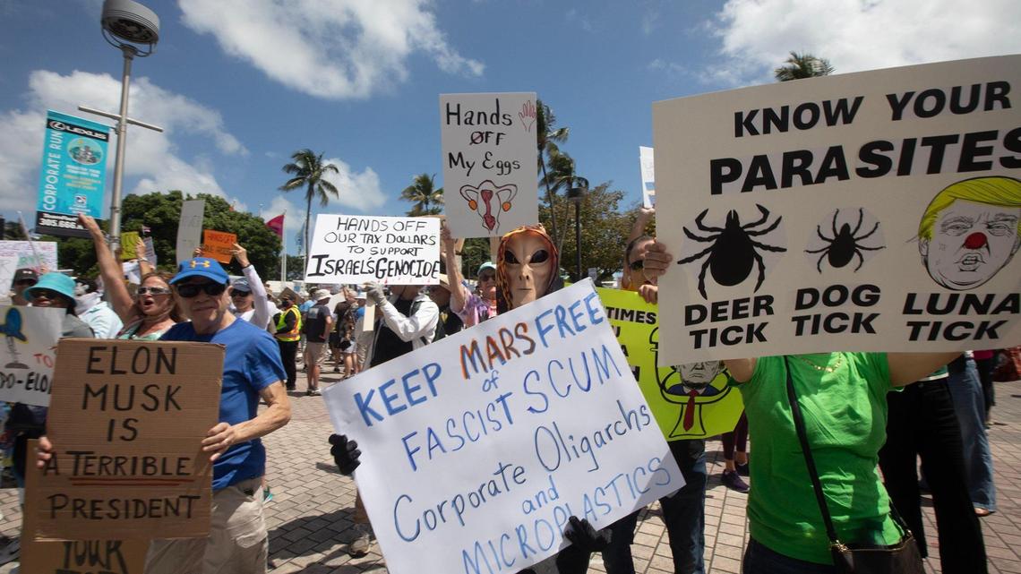 Protesters display signs near the Torch of Friendship in Miami during a protest against the policies of President Donald Trump and his advisor and supporter, billionaire Elon Musk. Thousands turned out in South Florida has part of nationwide day of demonstrations.