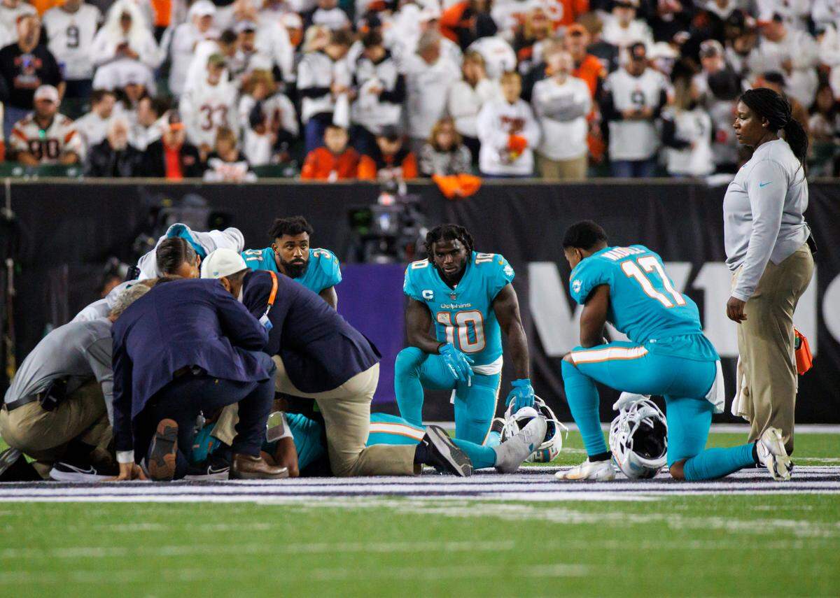 Los jugadores de los Miami Dolphins Raheem Mostert (31) Tyreek Hill (10) y Jaylen Waddle (17) se arrodillan junto a su compañero de equipo, el quarterback Tua Tagovailoa (1), mientras es atendido por el personal médico después de haber sido capturado atrás de la línea por el tackle defensivo de los Cincinnati Bengals Josh Tupou, durante el segundo cuarto de un partido de football de la NFL en el Paycor Stadium, el jueves 29 de septiembre de 2022 en Cincinnati, Ohio.