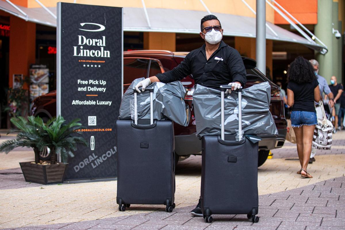 Rodrigo Taipe, 39, rolls a couple of suitcases with shopping bags on top while wearing personal protective equipment during Black Friday shopping at Dolphin Mall in Sweetwater, Florida, on Nov. 27, 2020.