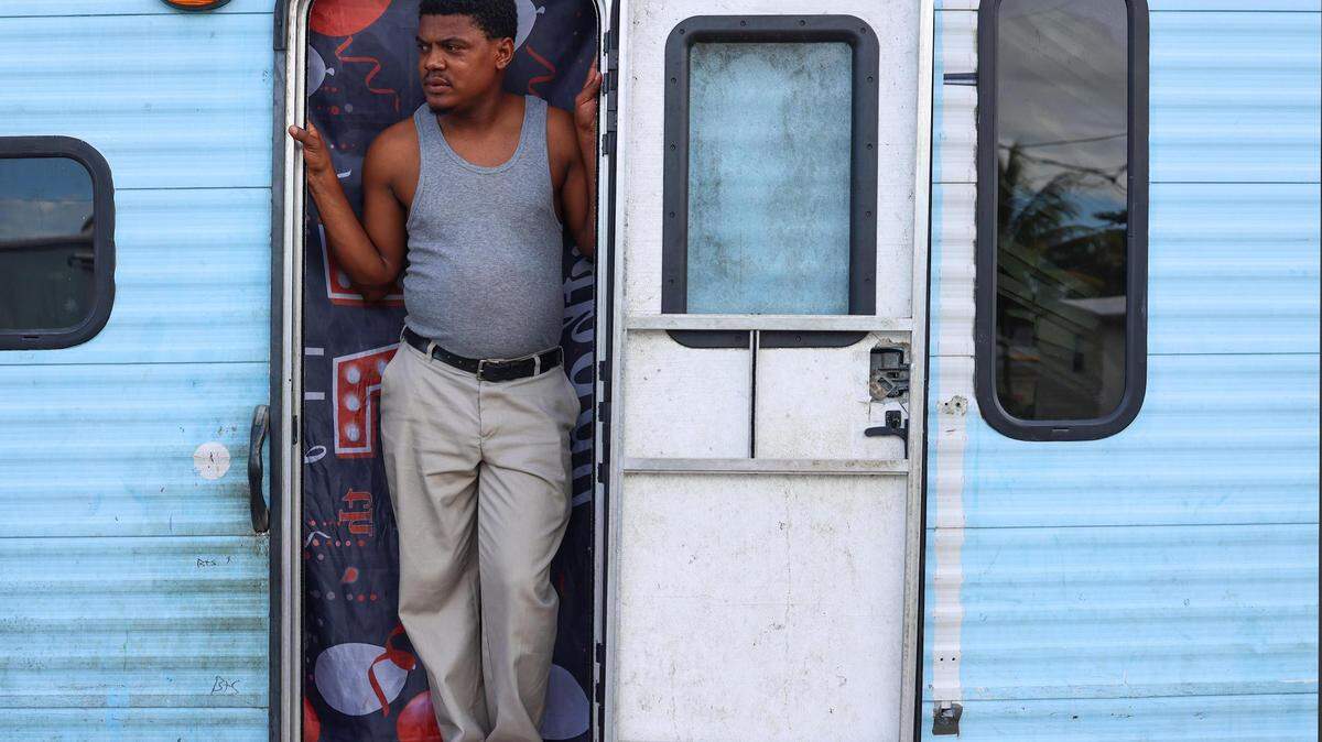 Diamenfull Destin, de 42 años y padre de tres, observa a sus hijos mientras juegan afuera de su casa móvil. Destin cría solo a sus hijos mientras su esposa permanece en Haití.