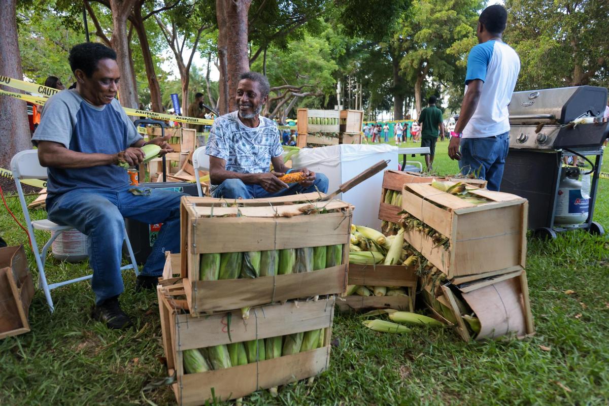 Hansy, center, watches how Gin, left, peels an ear of corn during the 19th annual Best of the Best International Music Festival at Bayfront Park in downtown Miami, Sunday, May 25, 2025.