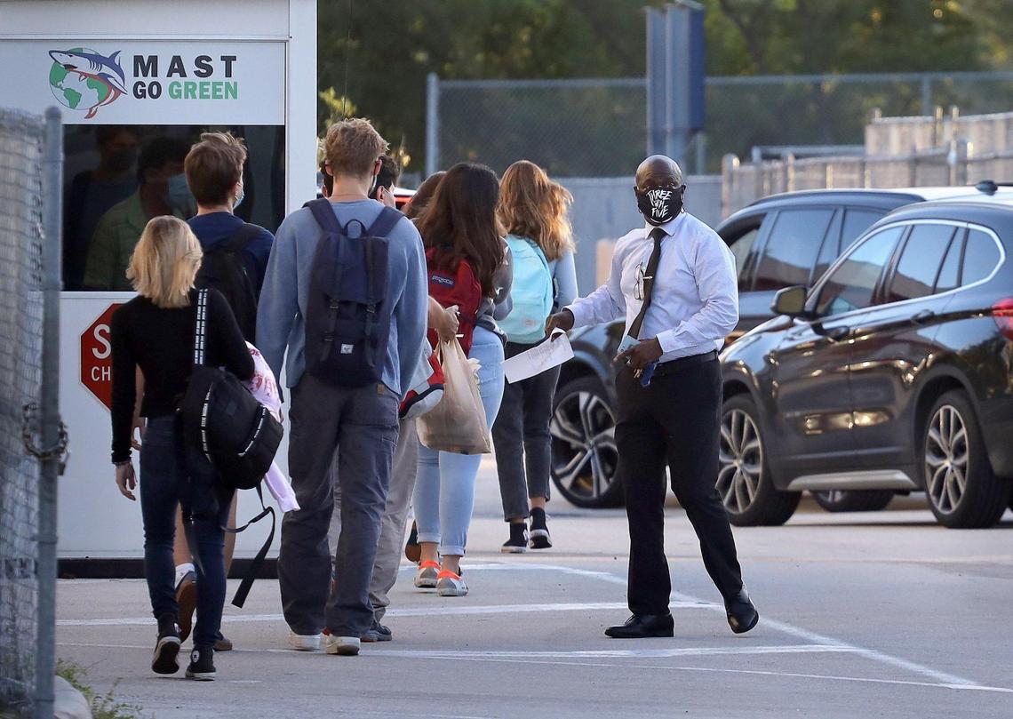 MAST Academy students walk toward campus while a school staffer guides cars toward the school drop-off point as Miami-Dade public schools’ elementary students plus students in grades 6, 9 and 10 returned for in-person learning on Wednesday, Oct. 7.