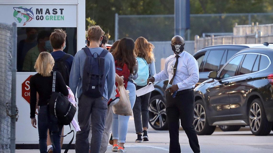 MAST Academy students walk toward campus while a school staffer guides cars toward the school drop-off point as all Miami-Dade public schools elementary students plus students in grades 6, 9 and 10 returned for in-person learning on Wednesday, Oct. 7. On the following Monday, Oct. 12, the school closed for the day due to two students testing positive for COVID-19.