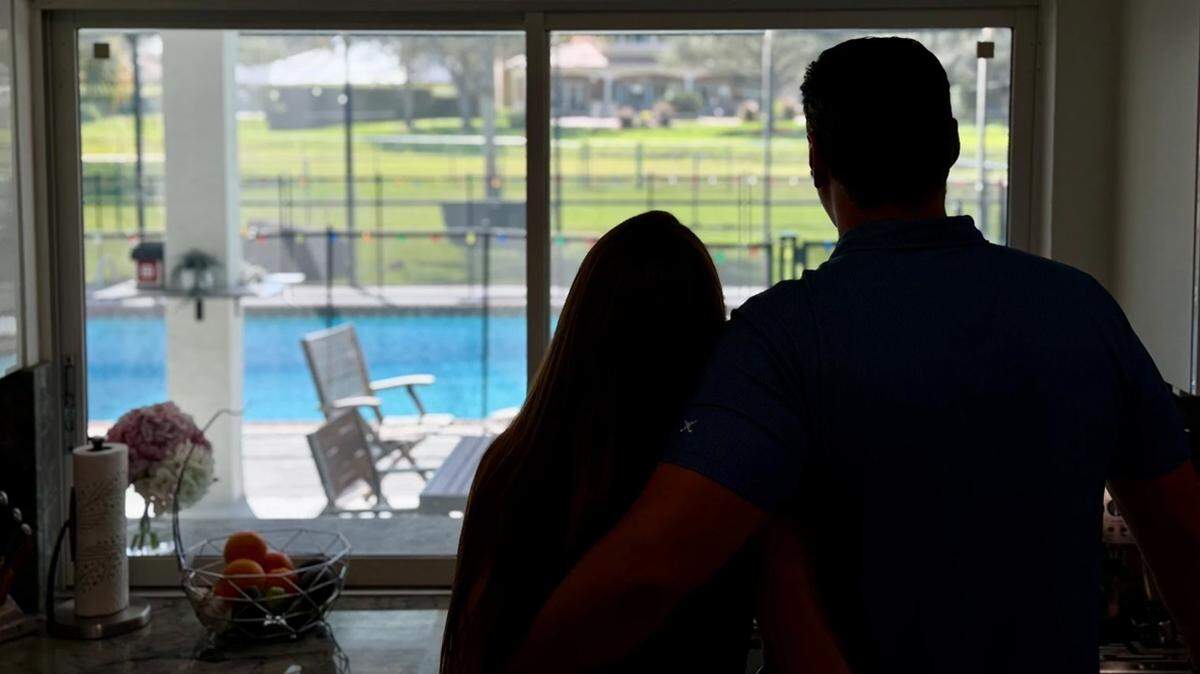 Michelle and Sean, not their real names, stand at their kitchen window in South Florida. Michelle was granted an H-1B visa as the couple pursues American citizenship.