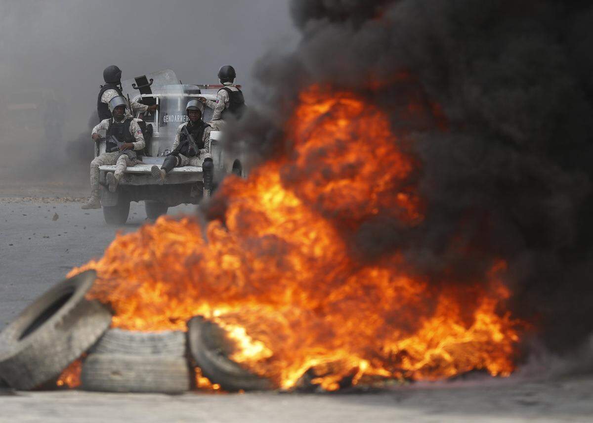 Police drive past burning tires lit by anti-government protesters on a road leading to the United Nations headquarters, in Port-au-Prince, Haiti, Friday, Oct. 4, 2019.