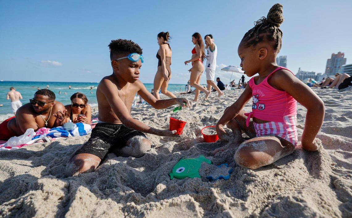 Noah Breaux and Sydney Breaux, play in the sand while their parents Andre and Farris Breaux sunbathe, at left, during spring break on Miami Beach, Florida on Friday, March 14, 2025.
