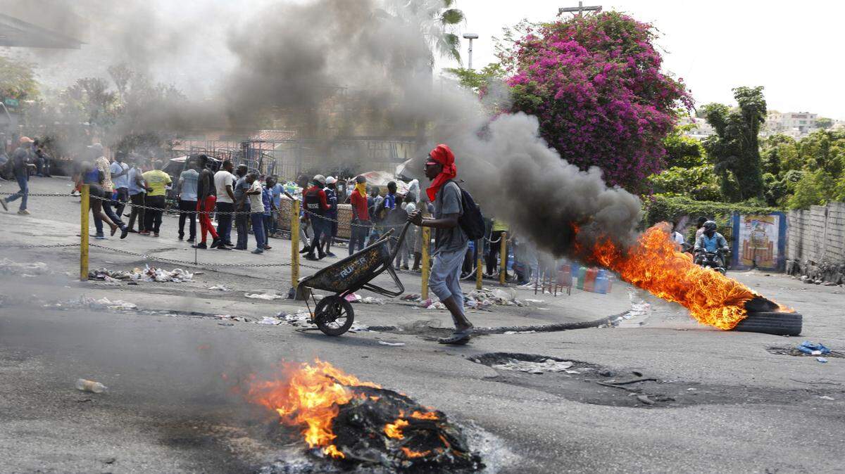 A man pushes a wheelbarrow past burning tires during a protest demanding the resignation of Prime Minister Ariel Henry, in Port-au-Prince, Haiti, Thursday, March 7, 2024. (AP Photo/Odelyn Joseph)