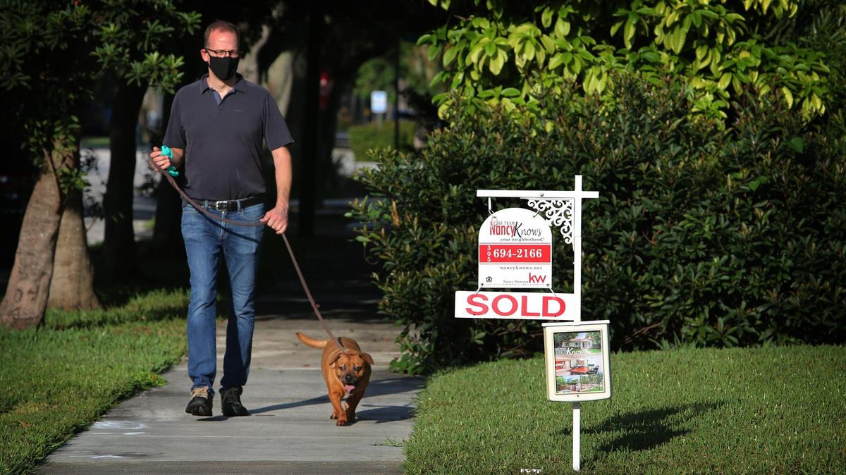 Miami Shores resident Shaun Rogers walks his dog, Astro, past a ‘Sold” sign hanging in the front yard of a home along NE 96th St. on September 30, 2020.