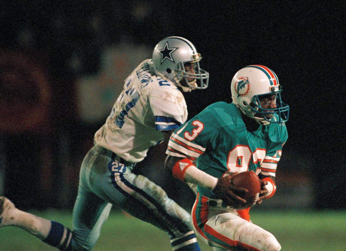 Miami Dolphin wide receiver Mark Clayton (83) takes a touchdown pass from Dan Marino ahead of Cowboys cornerback Ron Fellows (27) in the fourth quarter of action in Miami, Fla, Dec. 18, 1984. This reception tied an NFL touchdown reception record. (AP Photo/Joe Skipper)