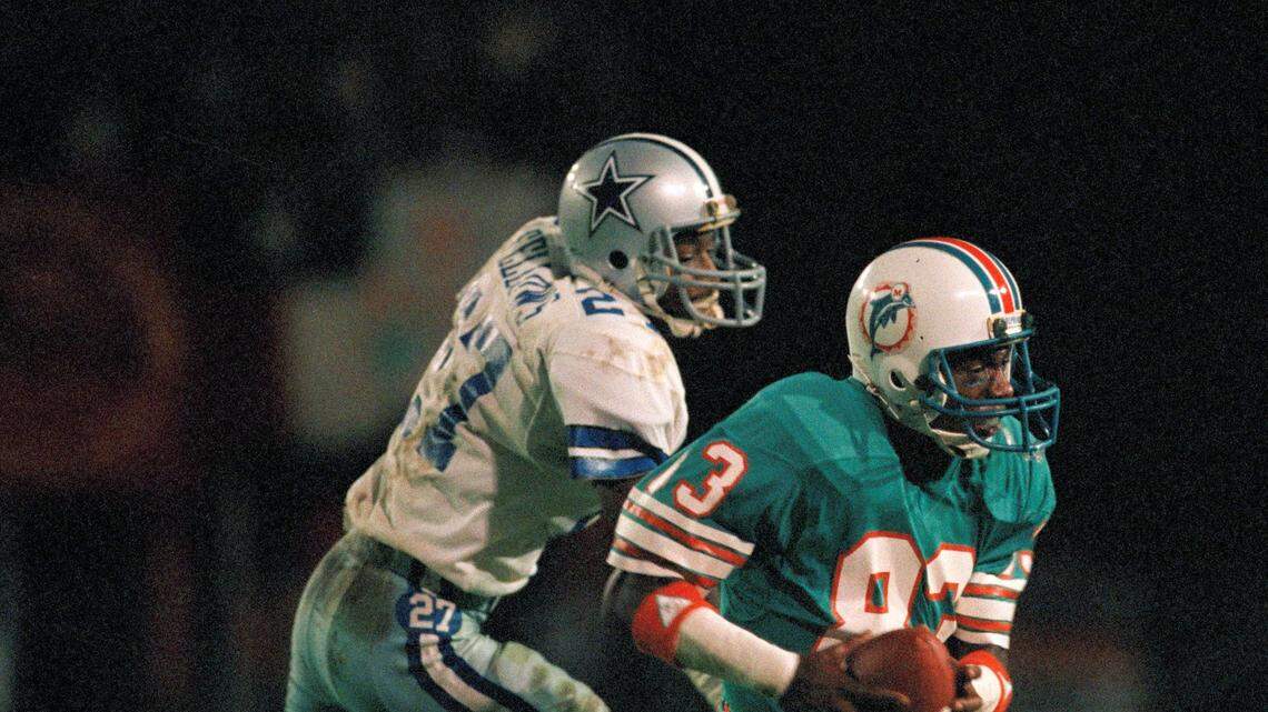 Miami Dolphin wide receiver Mark Clayton (83) takes a touchdown pass from Dan Marino ahead of Cowboys cornerback Ron Fellows (27) in the fourth quarter of action in Miami, Fla, Dec. 18, 1984. This reception tied an NFL touchdown reception record. (AP Photo/Joe Skipper)
