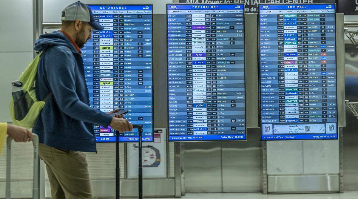 An information monitor shows departing and arriving flights with no cancellations at Miami International Airport on Friday, March 20, 2026, as a partial government shutdown causes TSA worker shortages and leads to long security lines nationwide.