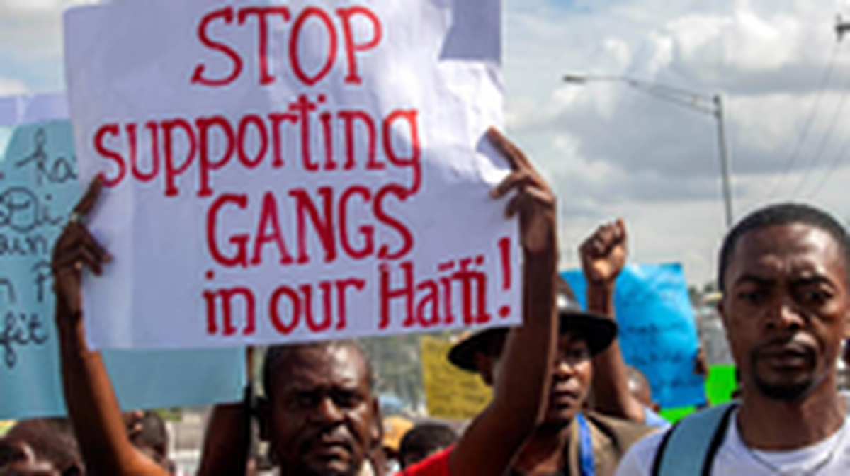 A protester in Port-au-Prince, Haiti, holds up a sign in 2020 demanding that support of violent gangs in Haiti end.