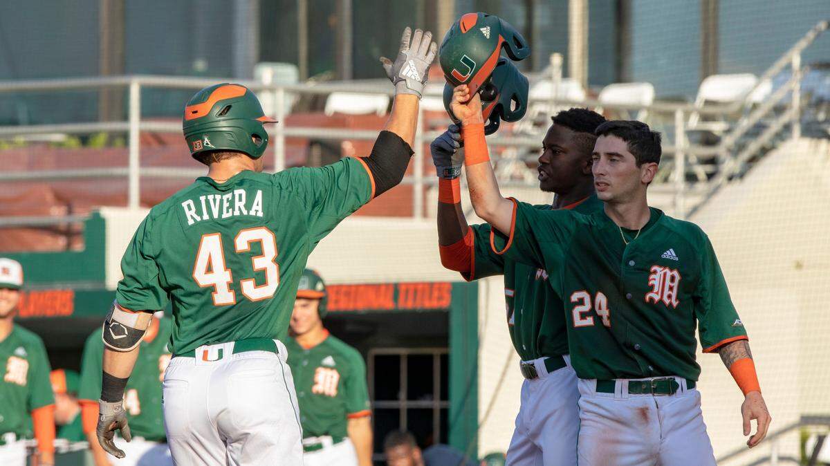Miami Hurricanes outfielder Gabe Rivera (43) celebrates at home plate with teammates Michael Amditis (24) and Tony Jenkins (51) after hitting a home run during the second inning of a baseball game against FIU at Alex Rodriguez Park in Coral Gables, Florida, on Wednesday, April 24, 2019.