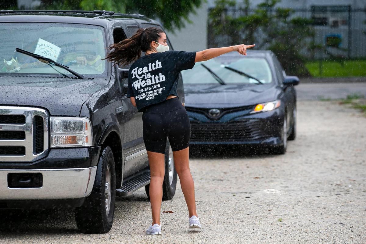 Joamna Ramirez directs cars during a drive thru distribution event in Miami’s Overtown neighborhood on Saturday, July 25, 2020. The Miami Foundation, Health Foundation of South Florida, Florida Blue Foundation and partners put nearly 70,000 units of PPE into the hands of 42 nonprofit organizations that got a three-month supply each to help fight the spread of COVID-19.