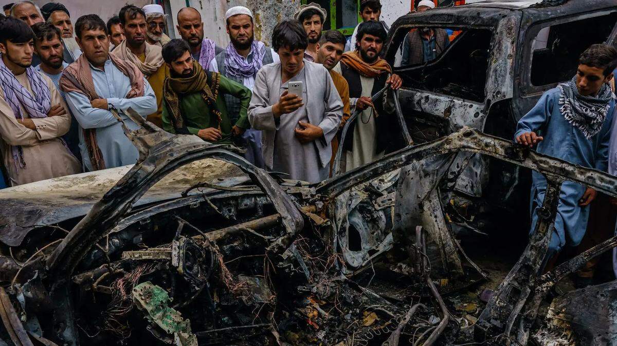 In August, relatives and neighbors of the Ahmadi family surround the incinerated shell of a vehicle targeted and hit by an American drone strike, in Kabul, Afghanistan.