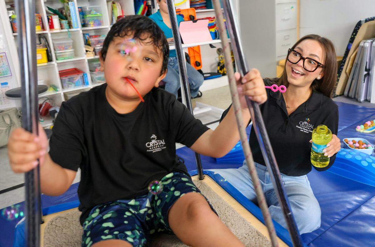 Speech language pathologist Julie Morales, right, uses motion and bubbles as a method of engagement with Benjamin Saez, 7, left, while sitting on swing as part of the sensory engagement. The Miami Herald was given tour of the school as it tries to continue to serve the needs of children with autistic students on Monday, September 23, 2025.
