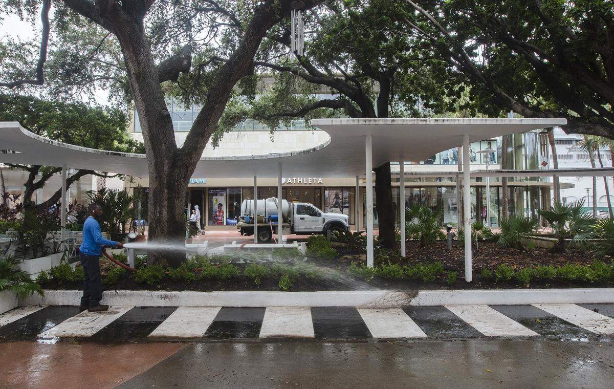 A Miami Beach employee washes off a curb along Lincoln Road Mall, where a long-delayed renovation now under way will restore and replenish the pedestrian street’s landscaping, water features and ‘follies’ — shade structures like the one seen here. Famed designer Morris Lapidus’ piano-keys design for the pavement, also seen here, will be reproduced with a more lasting application.