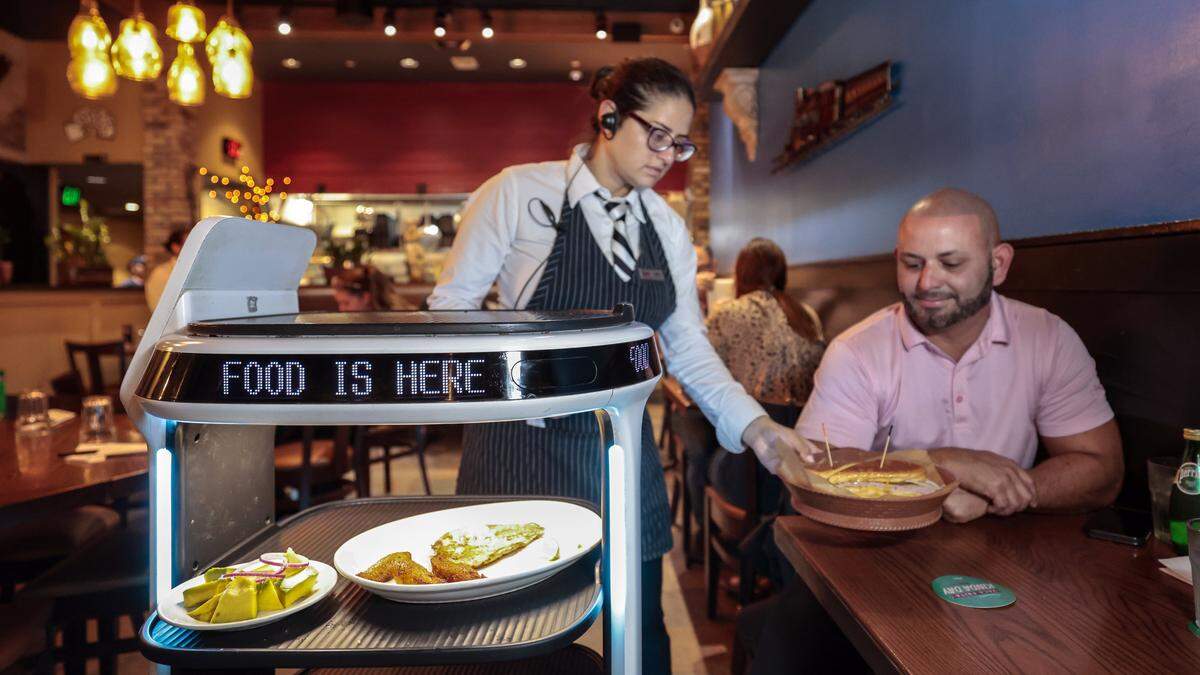 Server, Cecille Artigas, serves Alex Bustamante from a robotic food cart at Sergio's restaurant in Kendall. The local restaurant chain is celebrating it's 50th Anniversary in Miami, Florida, on Wednesday, September 24, 2025. 