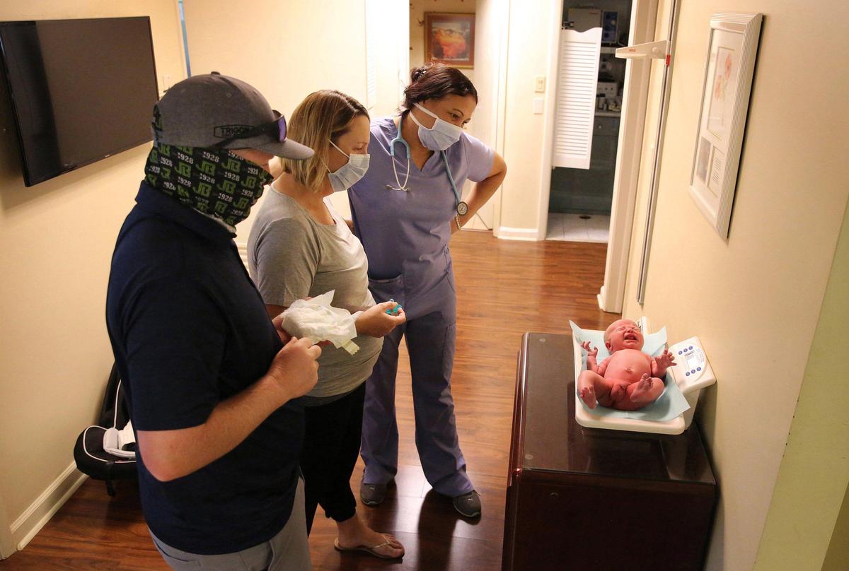 Tyler and Shauna Casey, of Miami Shores, and medical assistant, Collette Chin, look on as 12 day-old Lane Casey, is weighed during his very first newborn checkup on April 7, 2020 in the office of Dr. Keri Livingstone in Miami Shores.