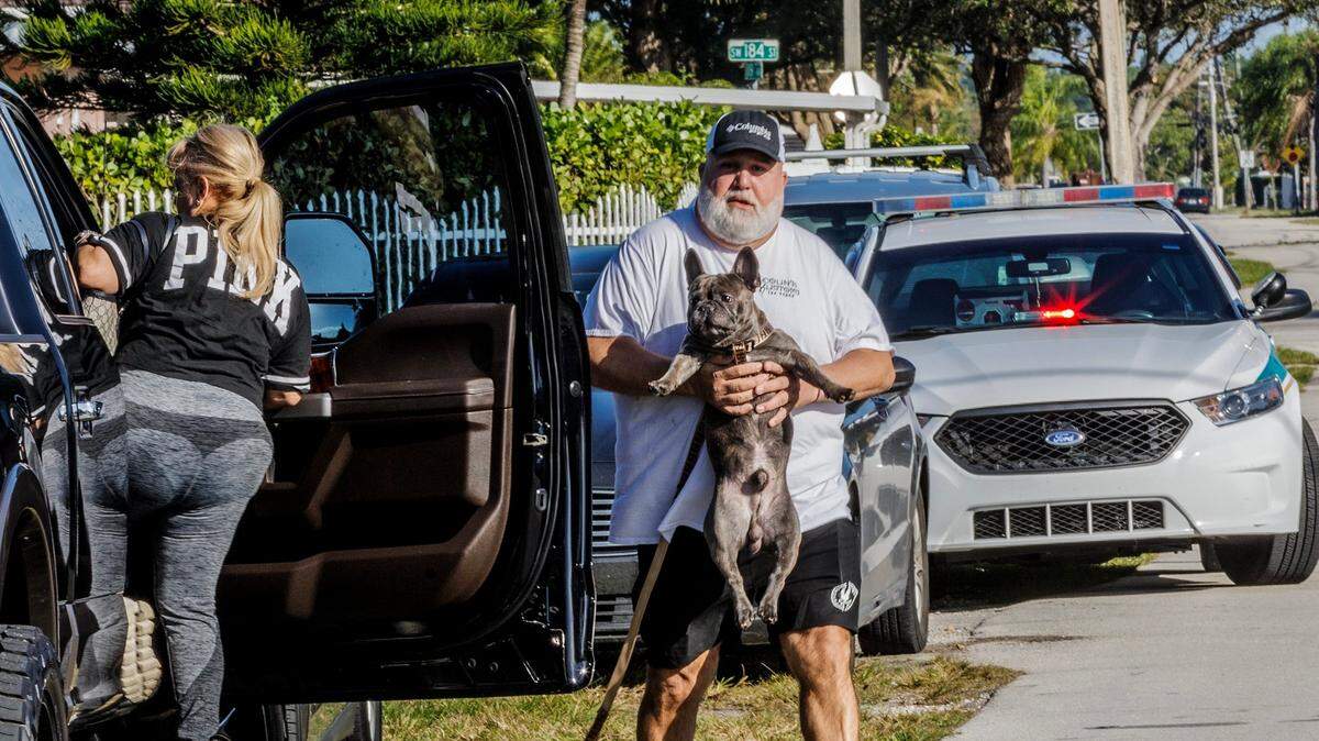 A man holding his dog approaches his car Saturday, January 27, 2024, after Miami-Dade County Police served a warrant on a house located at 11901 SW 185th Terrace that detectives say was used as an illegal veterinarian clinic.