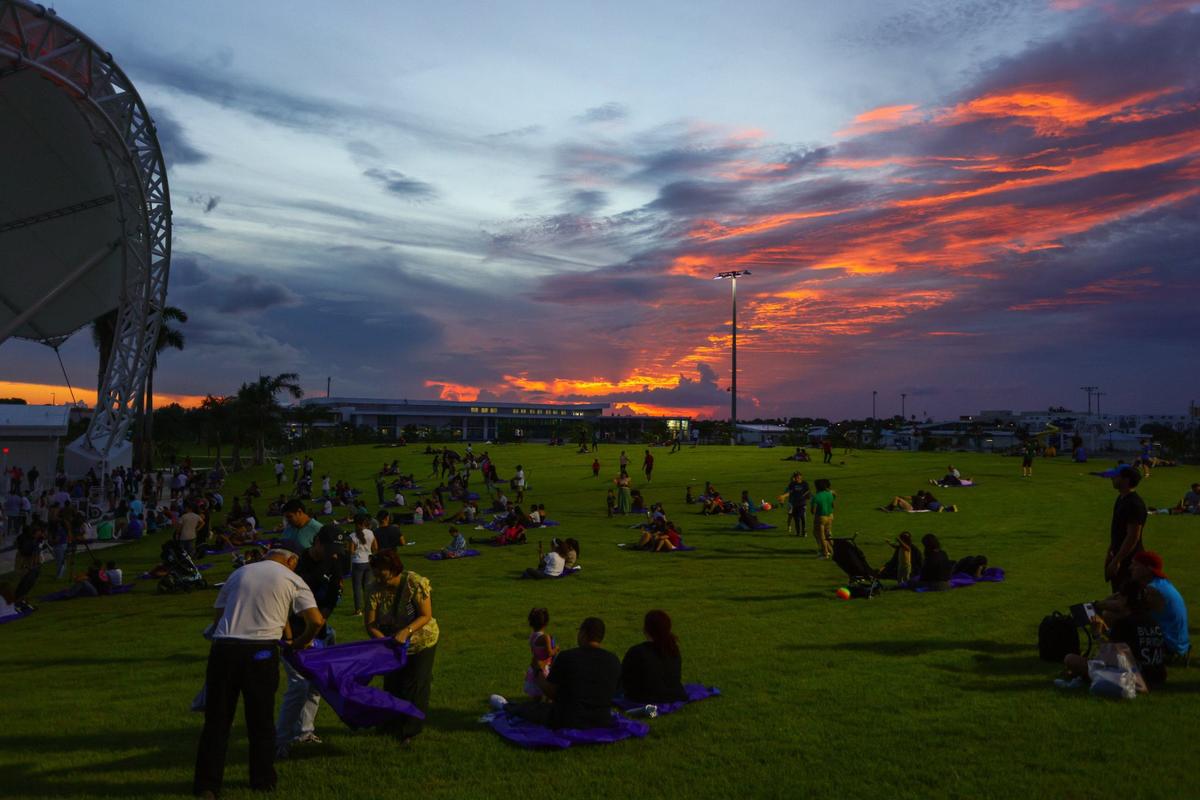 Asistentes a la inauguración del Doral Central Park disfrutan del césped del anfiteatro mientras se pone el sol durante la apertura de la parte este del Doral Central Park en 3005 NW 92nd Ave. en Doral, el parque más grande de la ciudad, el lunes 26 de agosto de 2024.