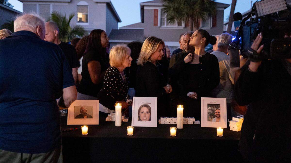 People walk past portraits of the victims of a triple homicide inside the Plum Bay community during a candle vigil on Sunday, February 23, 2025, in Tamarac, Florida.
