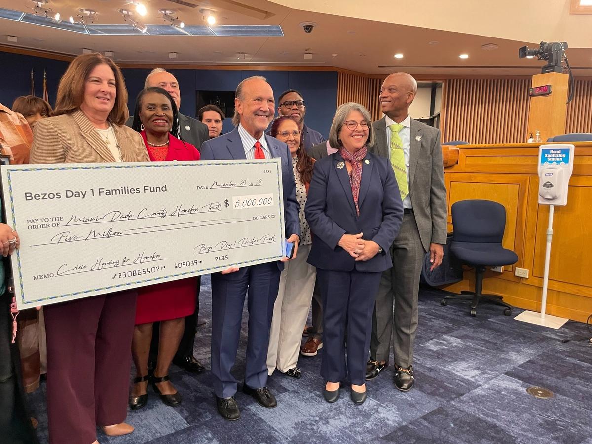 A foundation backed by Amazon founder Jeff Bezos and his fiancée, Lauren Sanchez, pledged $5 million to Miami-Dade County’s homeless services, run by the Homeless Trust. On Wednesday, Nov. 20, 2024, county leaders posed with a ceremonial jumbo check celebrating the gift. From left to right in the front row are: Victoria Mallette, director of the Homeless Trust; County Commissioner Marleine Bastien; Ron Book, chair of the Homeless Trust board; Mayor Daniella Levine Cava and County Commissioner Oliver Gilbert.