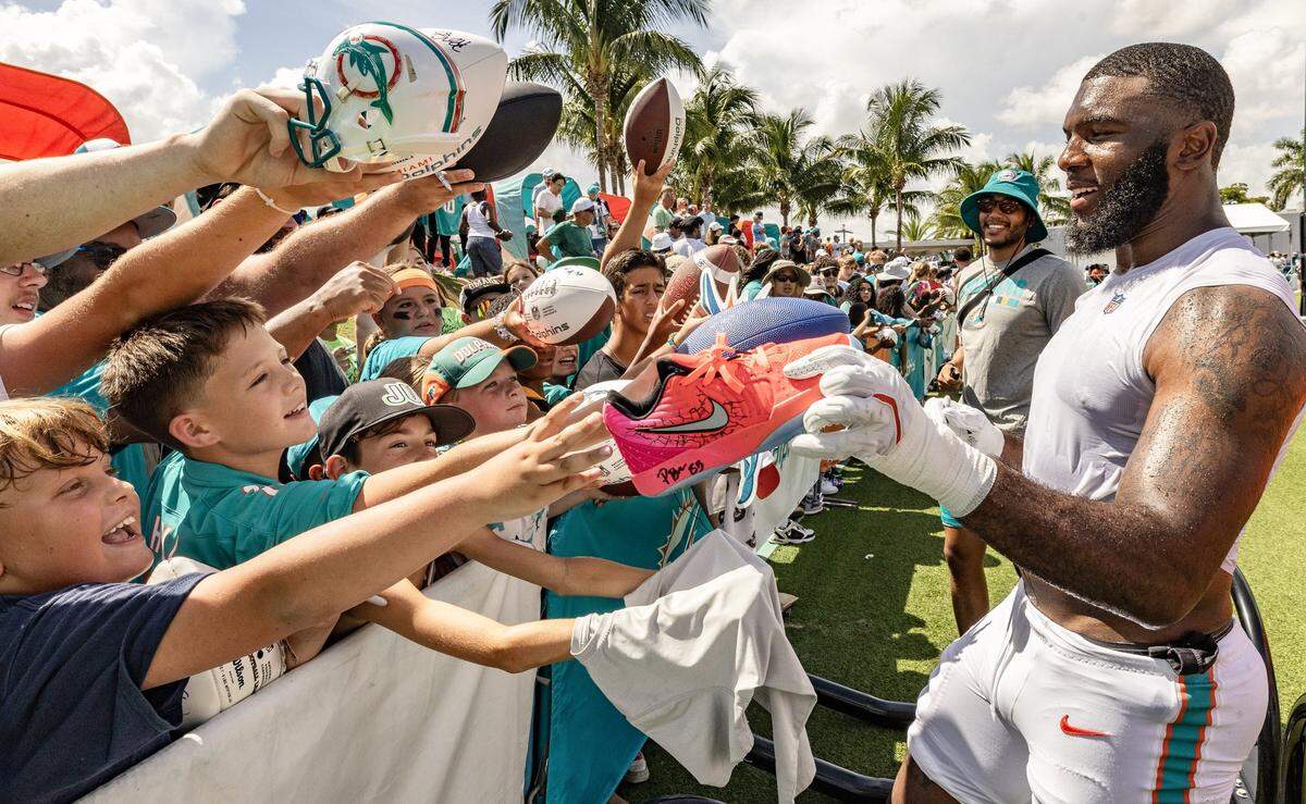 Miami Dolphins linebacker Dequan Jackson (57) grabs a shoe to autograph for a fan after practice.