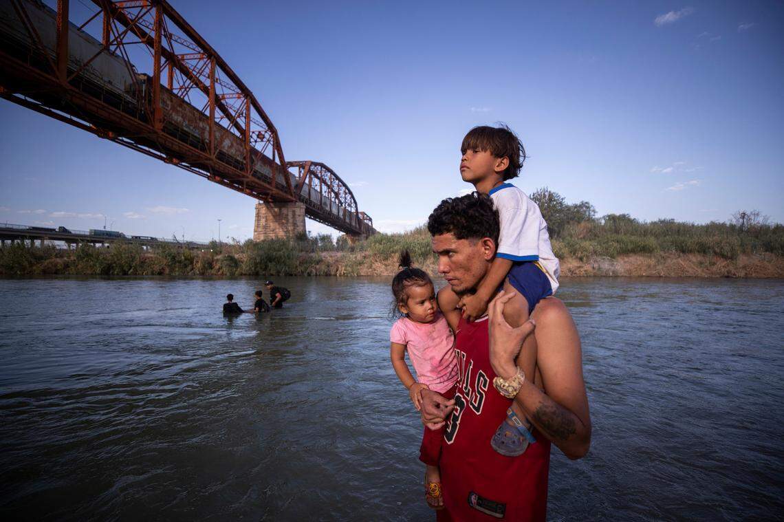 This file photo from July 2023 shows a migrant from Venezuela carrying his two young children as he looks back to Mexico as he waits for his wife as he crosses the Rio Grande River into the U.S. in Eagle Pass, Texas