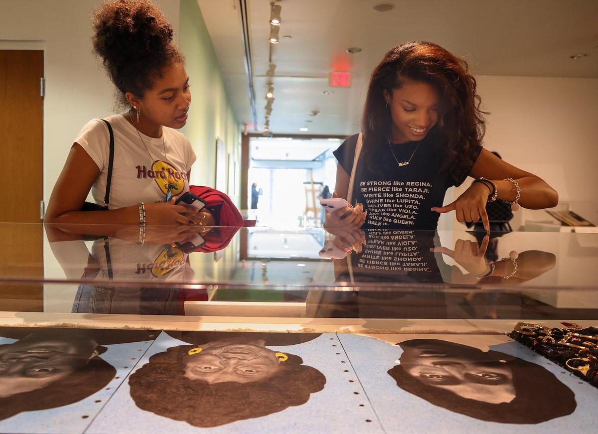 FIU students Loralei Gonzalez, left, and Nadia De La Mora, right, look at Chire Regans’ mixed-media piece ‘We Remember, We Remain.’