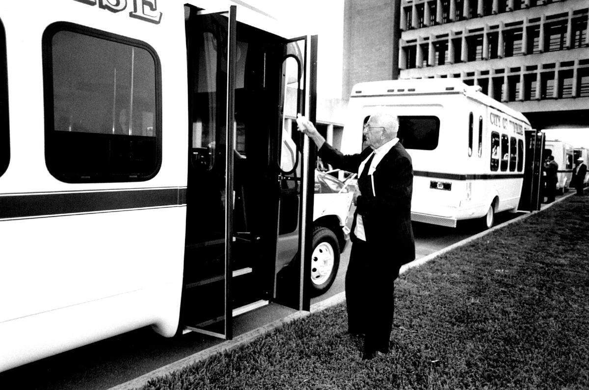 Father Albert Klein of St. Bernard Catholic Church blesses one of four new City of Sunrise buses with holy water during christening ceremonies out side of City Hall in 1992.