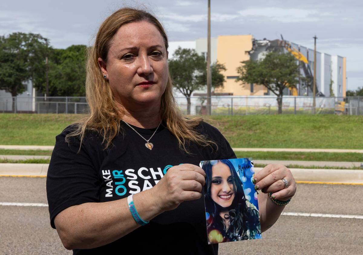 Lori Alhadeff holds a picture of her daughter, Alyssa, as crews use heavy equipment to tear down the 1200 building of Marjory Stoneman Douglas High School on Friday, June 14, 2024, in Parkland, Fla. Alhadeff’s 14-year-old daughter, Alyssa, was among the 17 people who died in the February 14, 2018, mass shooting at the school.