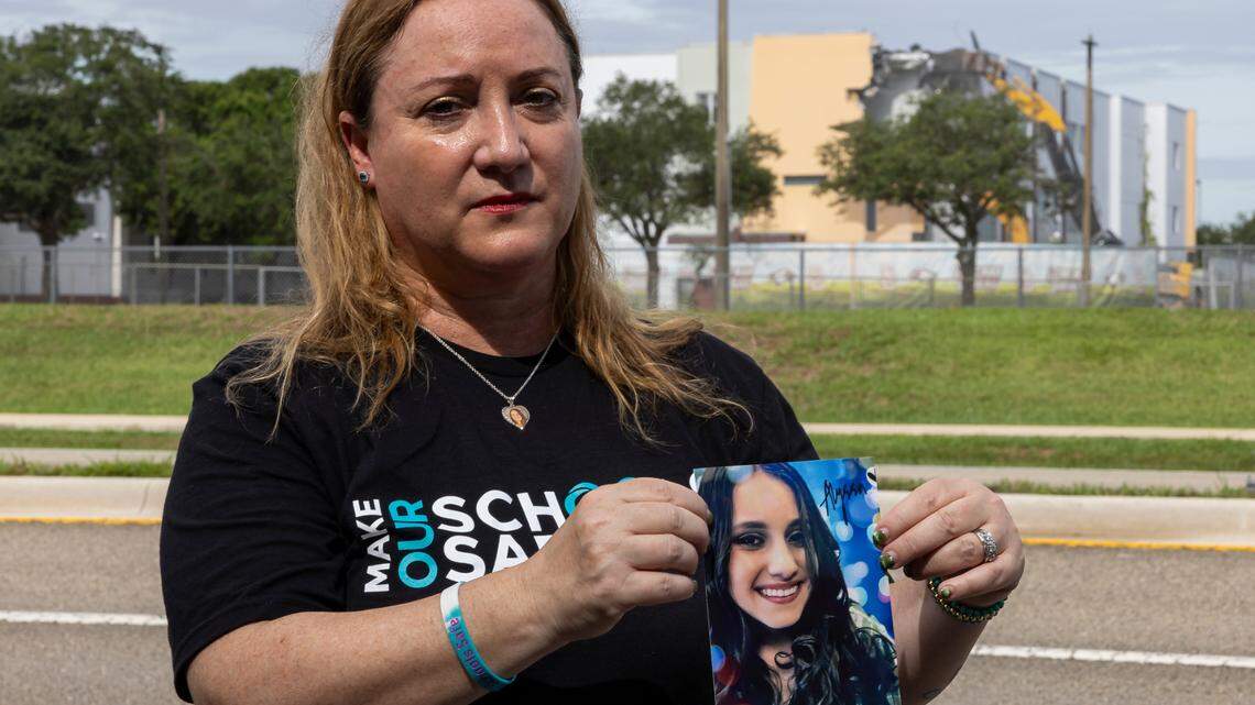 Lori Alhadeff holds a picture of her daughter, Alyssa, as crews use heavy equipment to tear down the 1200 building of Marjory Stoneman Douglas High School on Friday, June 14, 2024, in Parkland, Fla. Alhadeff’s 14-year-old daughter, Alyssa, was among the 17 people who died in the February 14, 2018, mass shooting at the school.