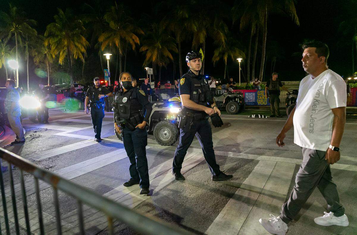 A group of police officers watch as TikTokers film a video on Ocean Drive and 8th Street in Miami Beach, Florida on Friday, March 25, 2022. City officials imposed a midnight curfew and forced stores to stop selling alcohol after 6 p.m. The restrictions were set in place after two shootings in Miami Beach the weekend before caused city officials to announce a “state of emergency.”